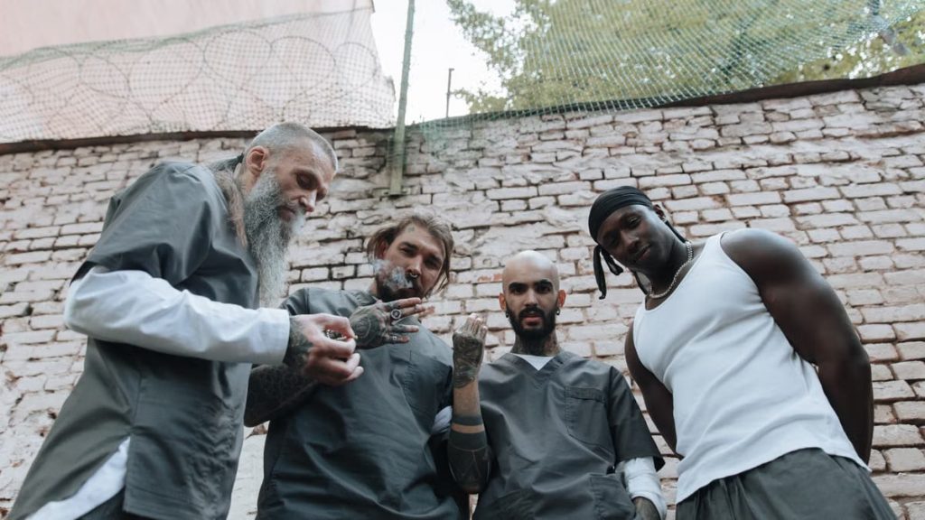 Four tattooed men standing near an outdoor brick wall, exuding a casual and confident vibe.